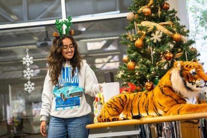 a student stands next to a Christmas tree with a toy Tiger in front of it